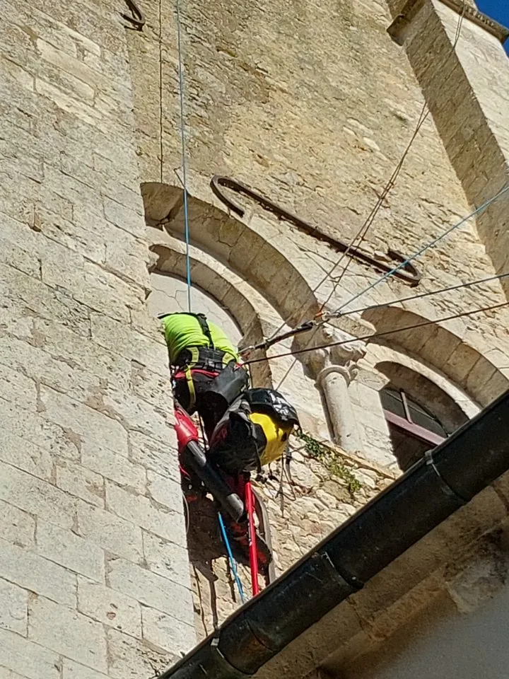 Cordiste en suspension contre la maçonnerie en pierre de l’église de Donnemarie-Dontilly, à proximité d’une toiture en tuiles.