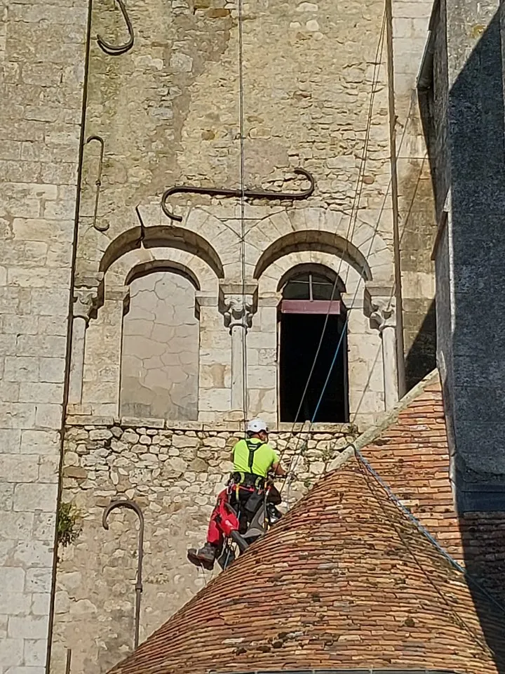 Cordiste sur un versant en tuiles, sous une ouverture du clocher de l’église de Donnemarie-Dontilly.