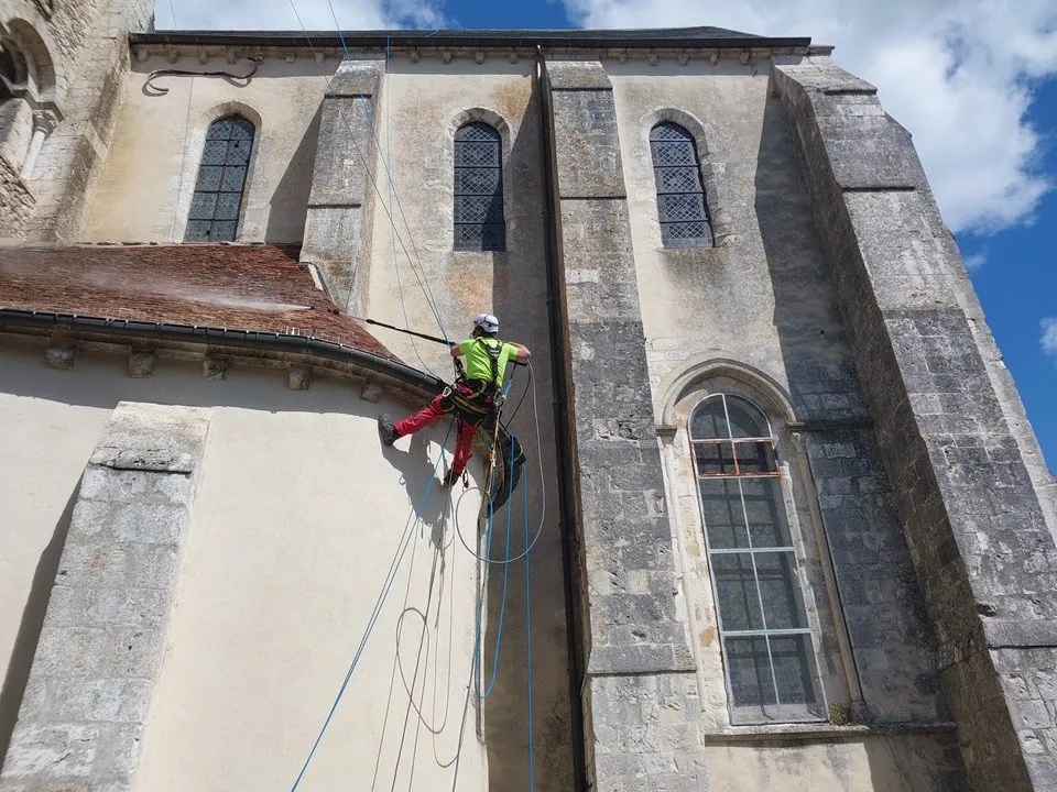 Cordiste travaillant au bord d’une toiture en tuiles de l’église de Donnemarie-Dontilly, avec ses cordes d’accès visibles.