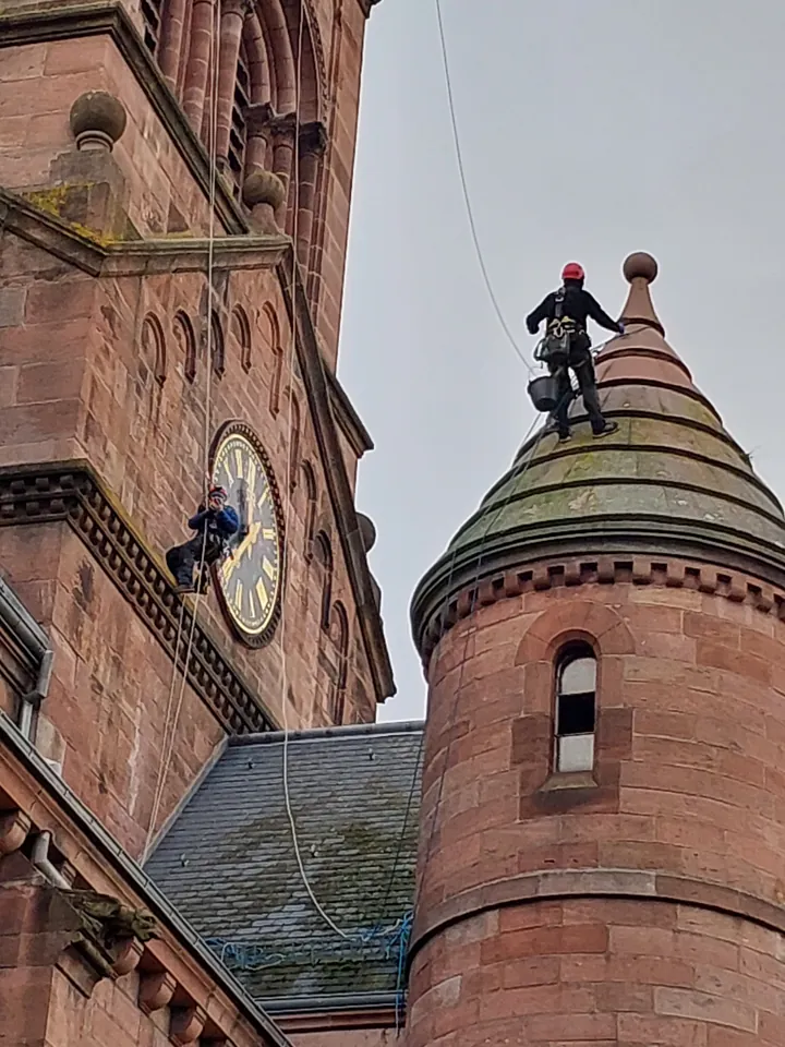 Cordiste au sommet d’une tourelle en grès, à côté de l’horloge de l’église protestante de Munster.
