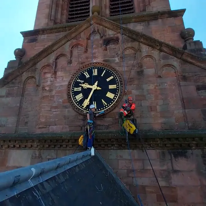 Cordistes en intervention devant la maçonnerie en grès et l’horloge de l’église protestante de Munster.